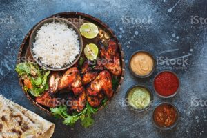 Tandoori chicken wings served with pilau rice,  soft garlic cheese naan with different chutney dipping sauces. Top view, blank space, rustic background