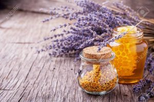 Arrangement of small glass jars with lavender honey, honeycombs and bee pollen with a bunch of dried lavender on dark wooden background. selective Focus