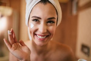 Beautiful smiling woman applying face cream in the bathroom.