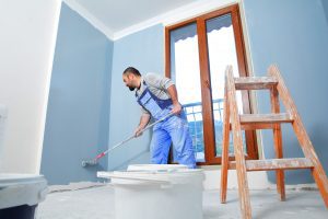 Painter man at work takes the color with paint roller from the bucket. With copy space