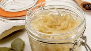 sauerkraut in a glass jar with bayleaf and a spoon with juniper berries