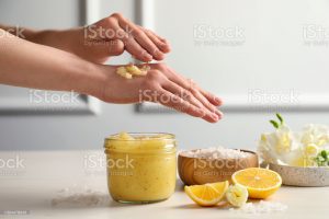 Woman applying body scrub on hand at wooden table, closeup